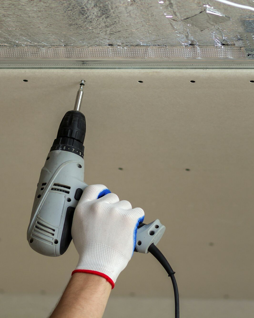 Worker hand with screwdriver connecting suspended drywall ceiling to metal frame. Renovation